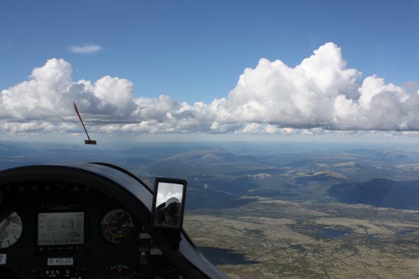 From a glider cockpit high over Norwegian mountains, a line of cumulus ahead and the yaw string on the canopy.