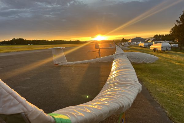 Gliders in their covers along the flightline at sunset, wings catching the last of the light.